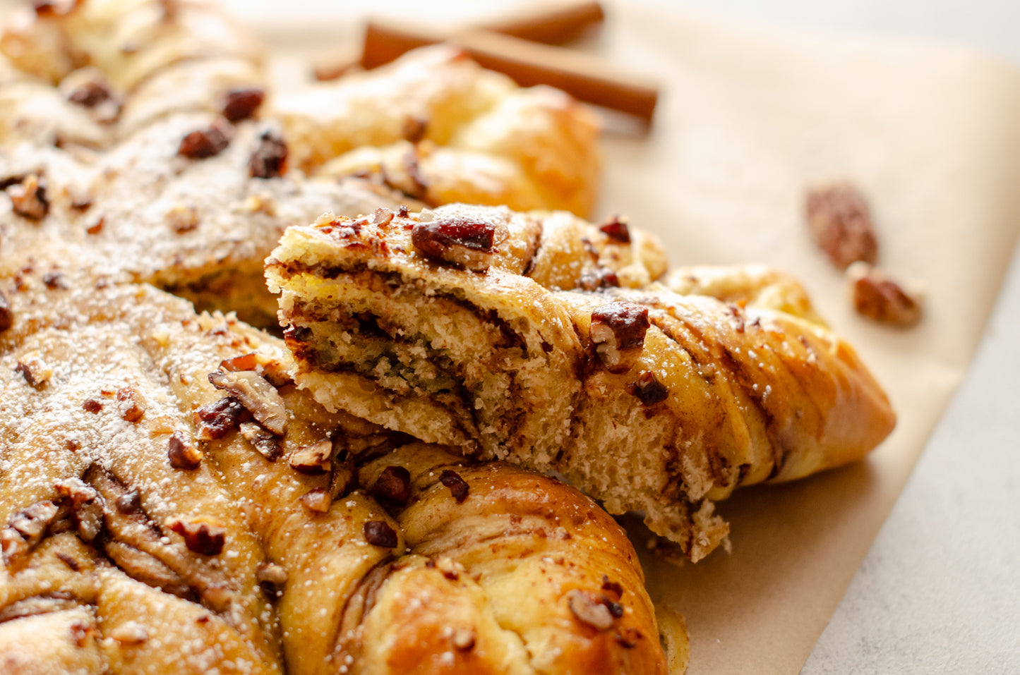 Close up of a slice of the Chocolate Pecan Snowflake bread showing the layers of hazelnut chocolate swirled between layers of sweet bread, dusted with powdered sugar and sprinkled with candied pecans - resting on brown paper, baked fresh for the holidays by Chillable Bake Shop in Darien, WI.