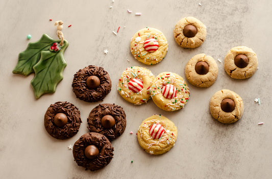 Assorted Holiday Blossom Cookies with chocolate kisses and candy decorations on a textured surface with a ceramic holly ornament, baked fresh in Darien, WI by Chillable Bake Shop.