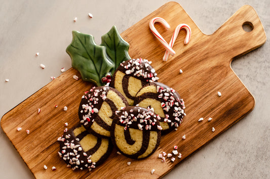 Decorative red and white peppermint pinwheel cookies arranged on a wooden tray with holly and candy cane decorations, fresh from Chillable Bake Shop in Darien, Wisconsin.