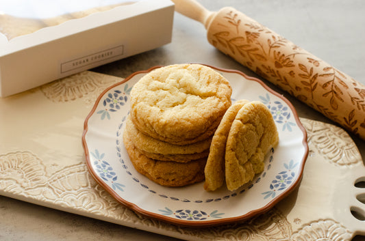 Stack of classic sugar cookies with a soft, buttery texture on a decorative plate with a rolling pin and box in the background, fresh-baked by Chillable Bake Shop in Darien, WI.