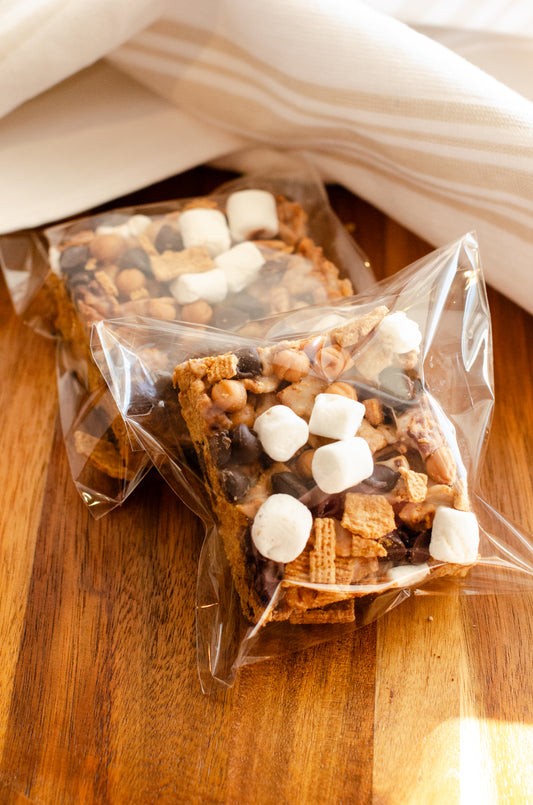 S’mores Rice Krispie treats topped with chocolate and marshmallows in clear packaging on a wooden surface, fresh-made in Darien, Wisconsin.
