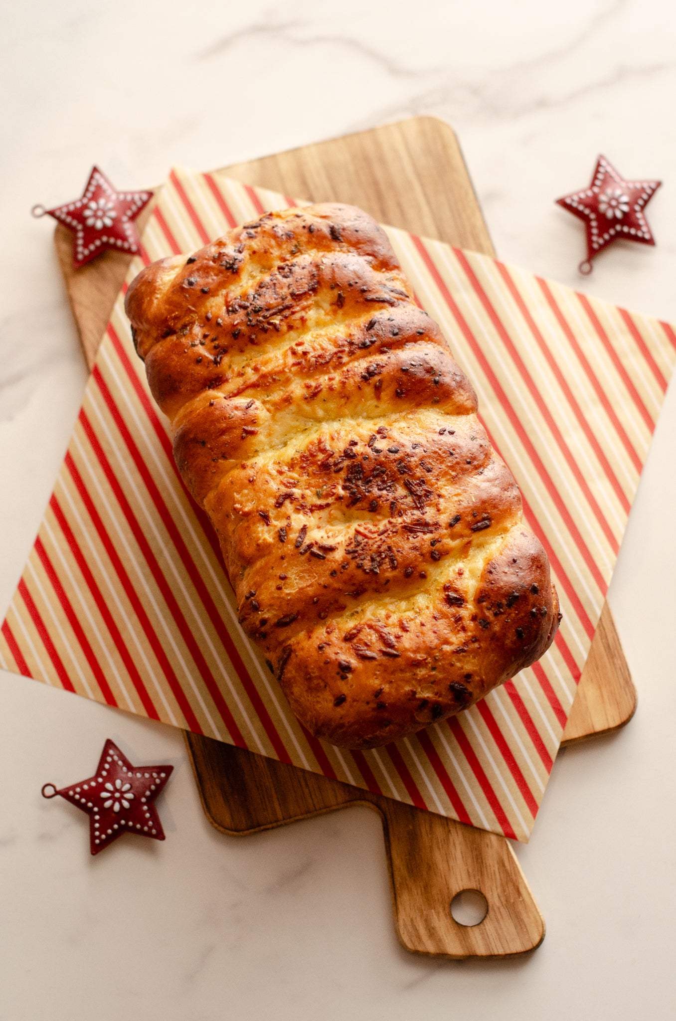 Golden garlic parmesan butter bread loaf topped with herbs on a wooden cutting board with red and white striped paper underneath, on a light background, baked fresh by Chillable Bake Shop in Darien, Wisconsin. 