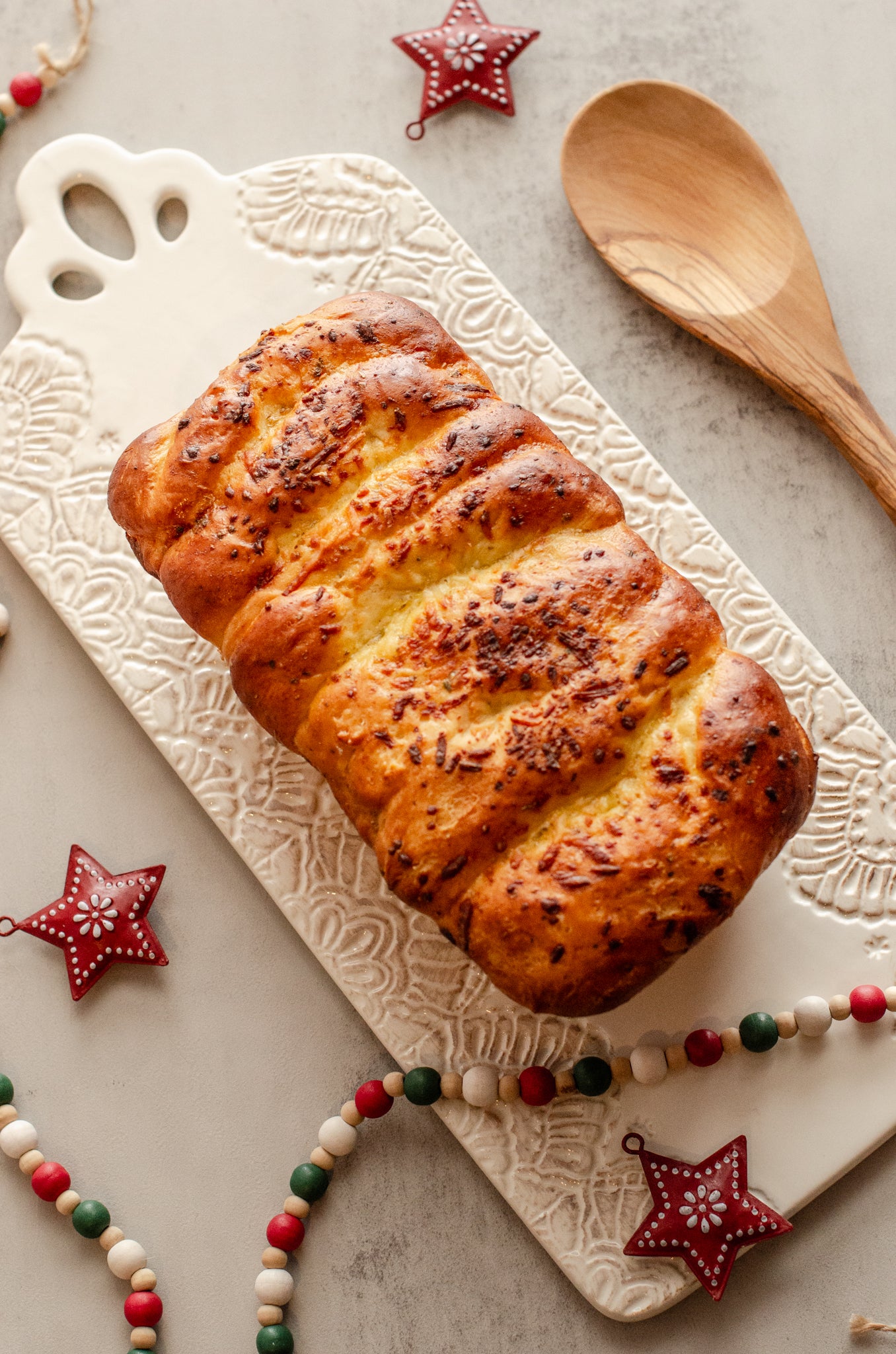 Golden garlic parmesan butter bread loaf topped with herbs on a decorative cutting board with Christmas decorations, baked fresh by Chillable Bake Shop in Darien, Wisconsin.