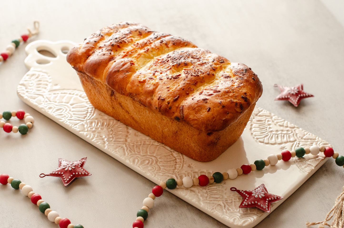 Golden garlic parmesan butter bread loaf topped with herbs on a decorative cutting board with Christmas decorations, baked fresh by Chillable Bake Shop in Darien, Wisconsin.