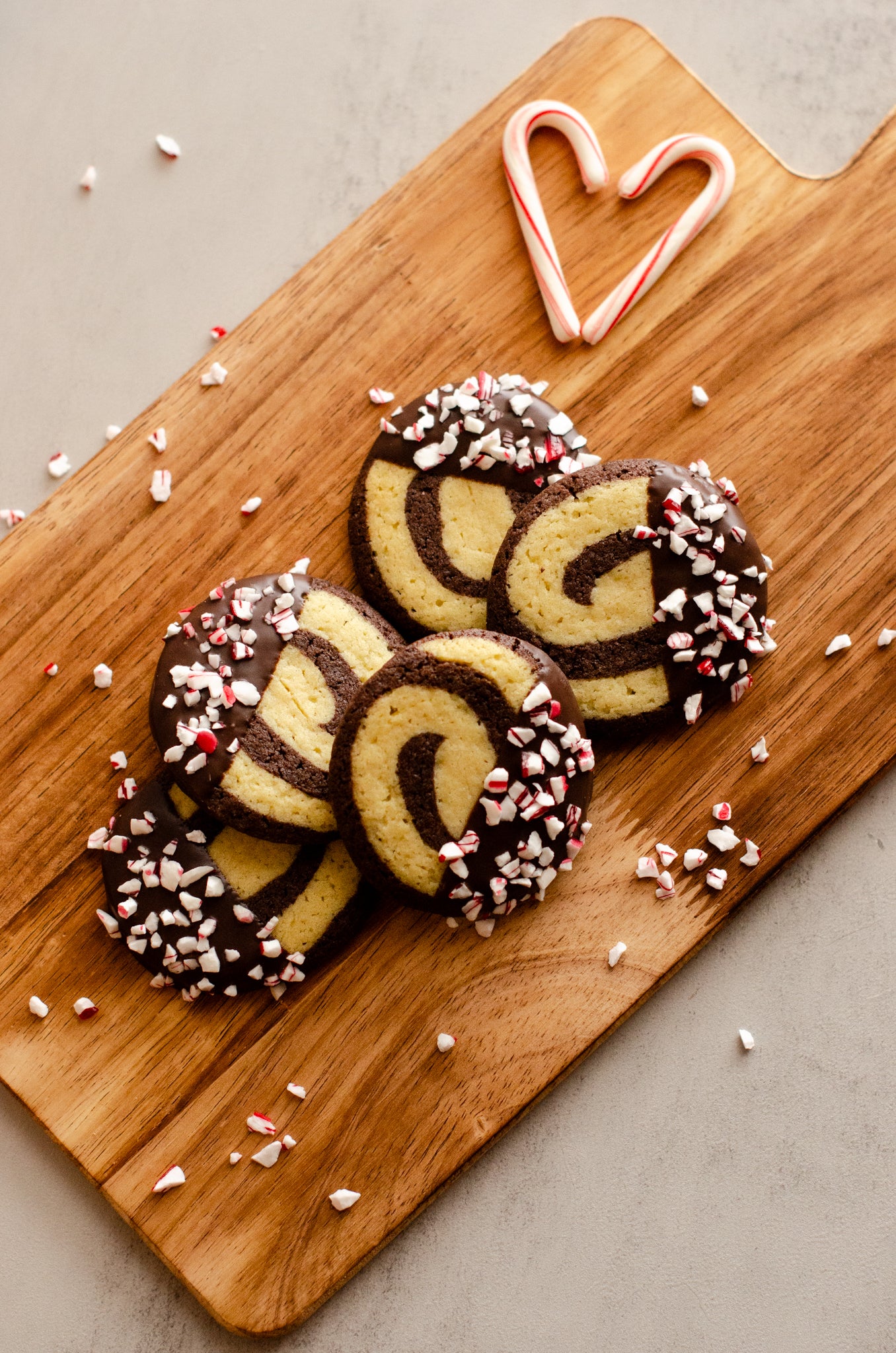 Decorative red and white peppermint pinwheel cookies arranged on a wooden tray with candy canes shaped like hearts, fresh from Chillable Bake Shop in Darien, Wisconsin.