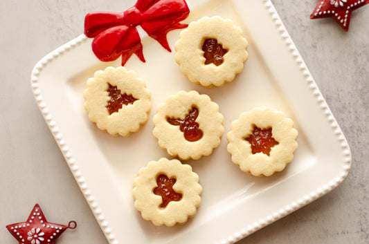 Peach nutmeg shortbread Linzer cookies with cutout centers on a white plate with a red bow, on a gray surface with Christmas decorations. Baked fresh by Chillable Bake Shop in Darien, WI. 