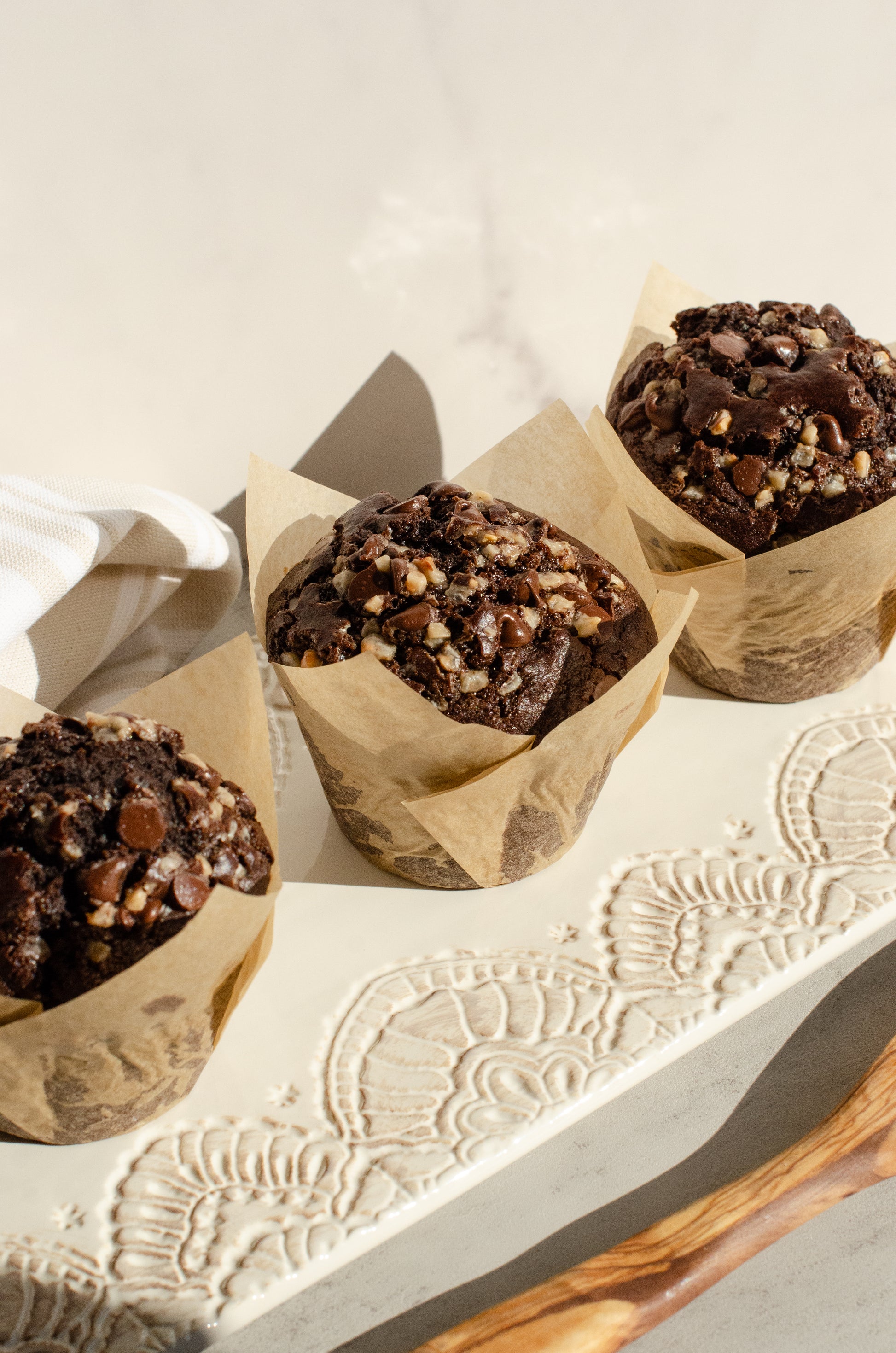 Three Mocha muffins with chocolate and espresso flavors in brown paper cups on a textured surface, baked by Chillable Bake Shop in Darien, Wisconsin.