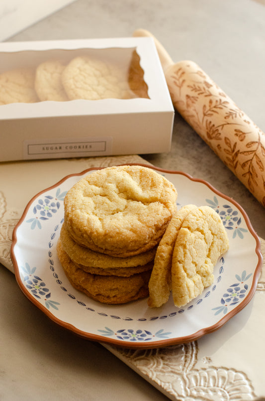 Stack of classic sugar cookies with a soft, buttery texture on a decorative plate with a rolling pin and box in the background, fresh-baked by Chillable Bake Shop in Darien, WI.