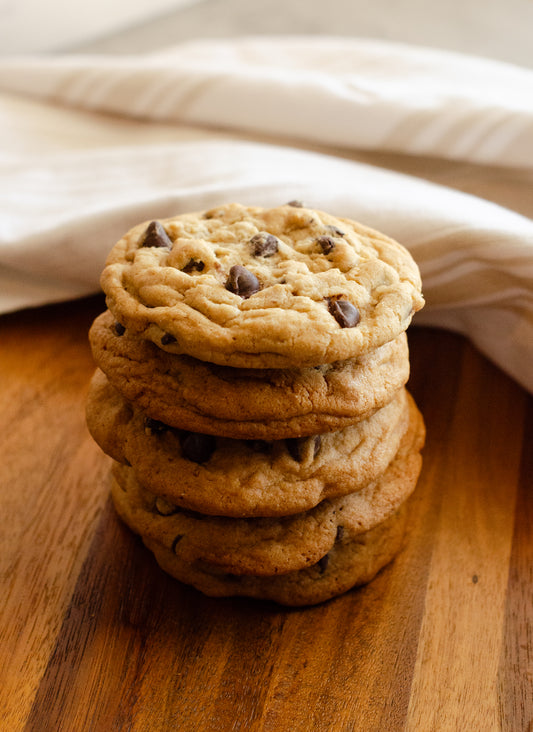 Stack of soft, chewy, chocolate chip cookies on a wooden surface with a white cloth in the background , baked fresh by Chillable Bake Shop in Darien, Wisconsin.