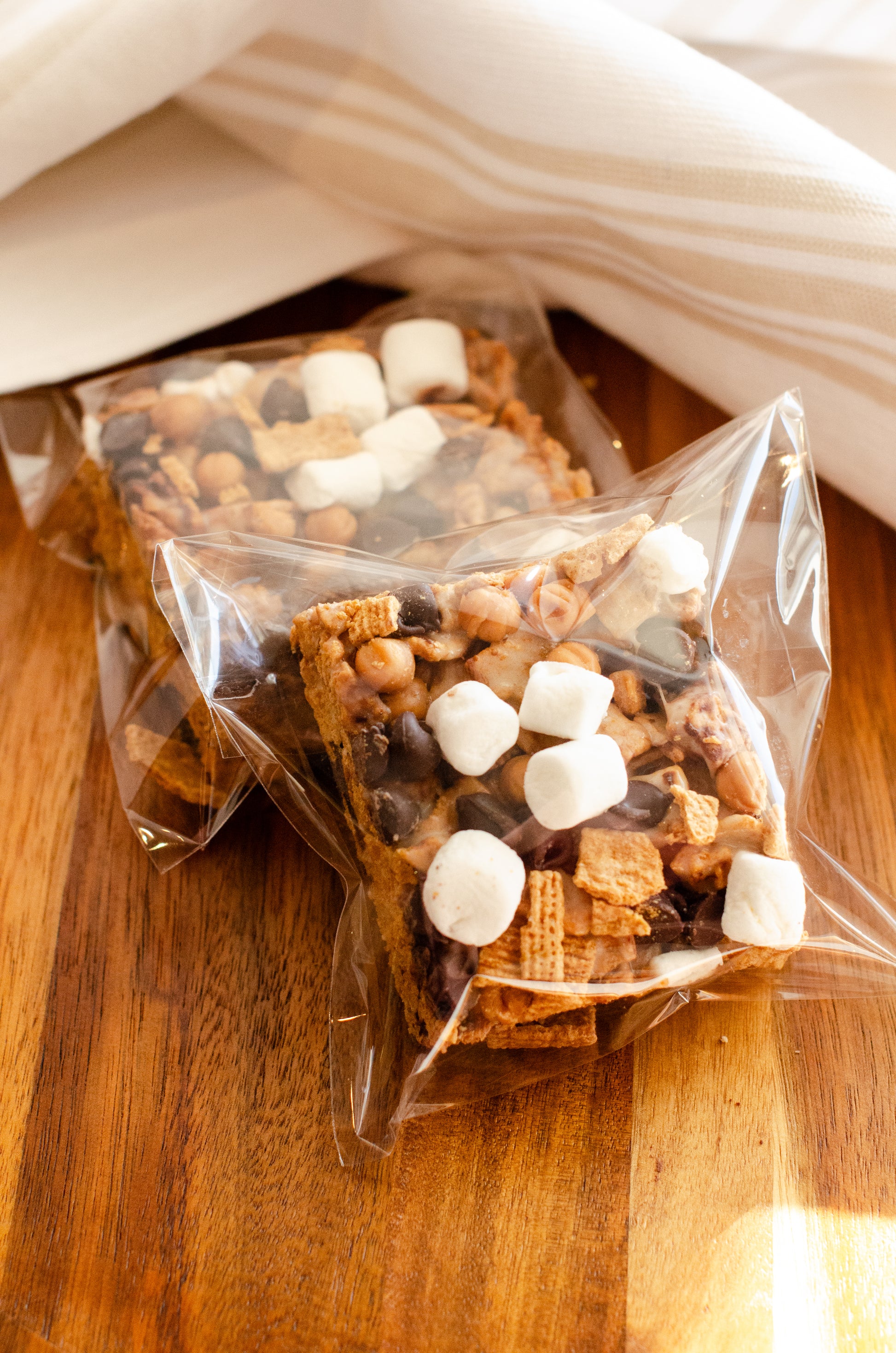 S’mores Rice Krispie treats topped with chocolate and marshmallows in clear packaging on a wooden surface, fresh-made in Darien, Wisconsin.